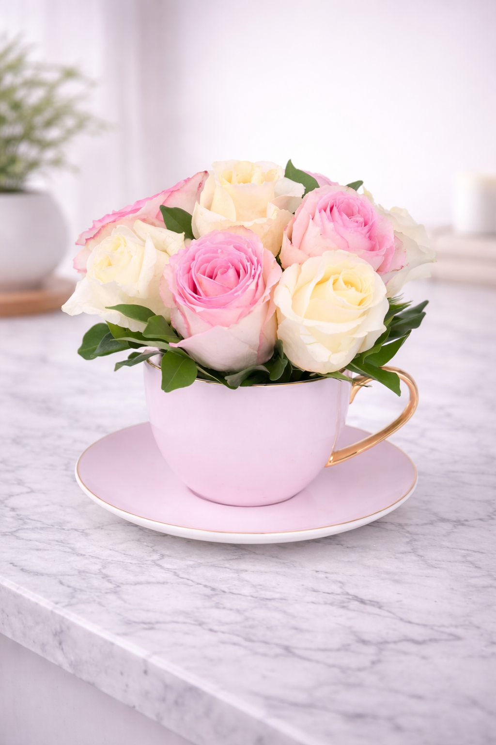 Pink teacup filled with pink and white roses on a marble surface