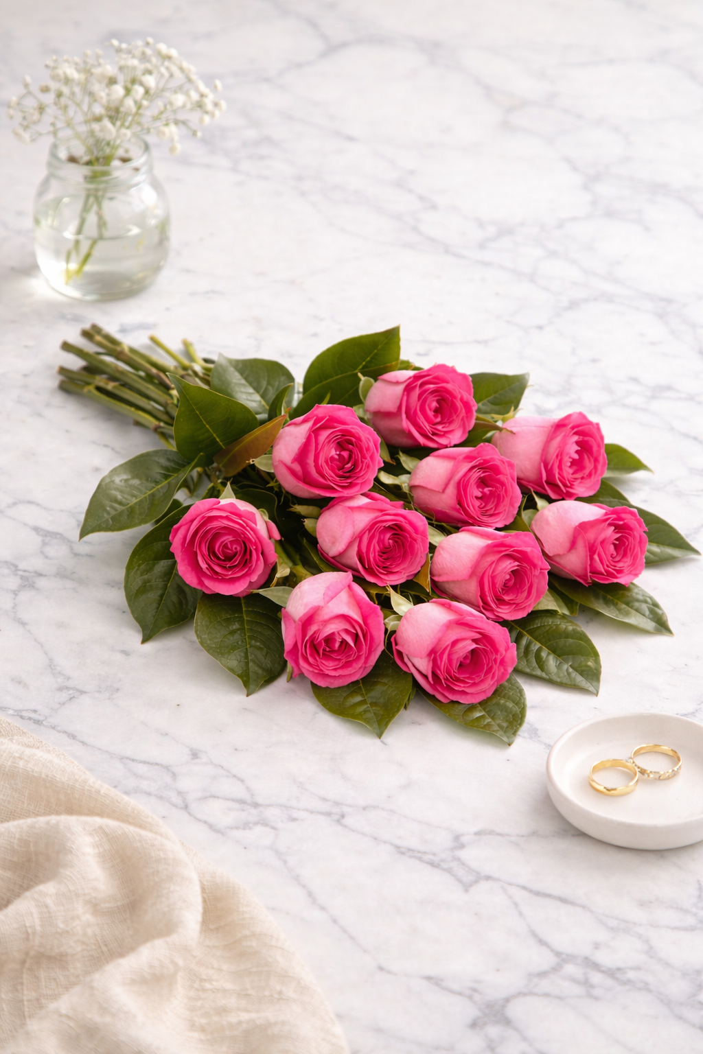 Bouquet of pink roses on a marble surface with a small vase and rings.