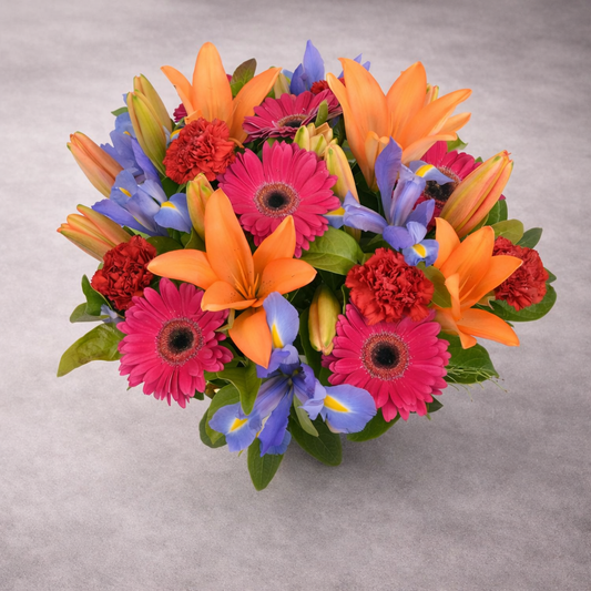 Colorful bouquet of flowers including orange lilies, pink gerberas, and blue irises on a gray background