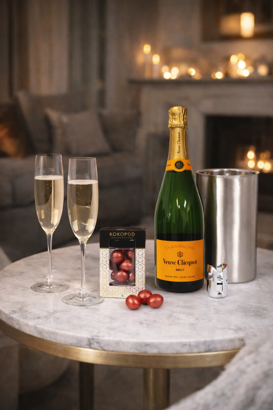 Bottle of Veuve Clicquot champagne with two glasses and a box of chocolates on a marble table.