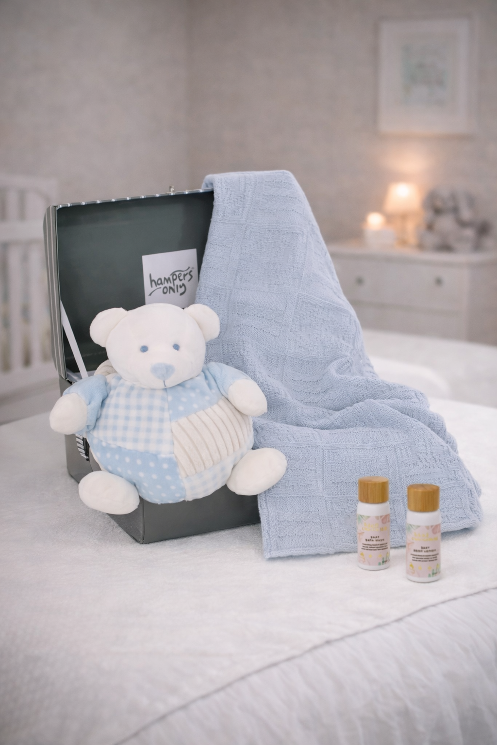 Baby gift set with blue teddy bear, blanket, and bottles on a bed.