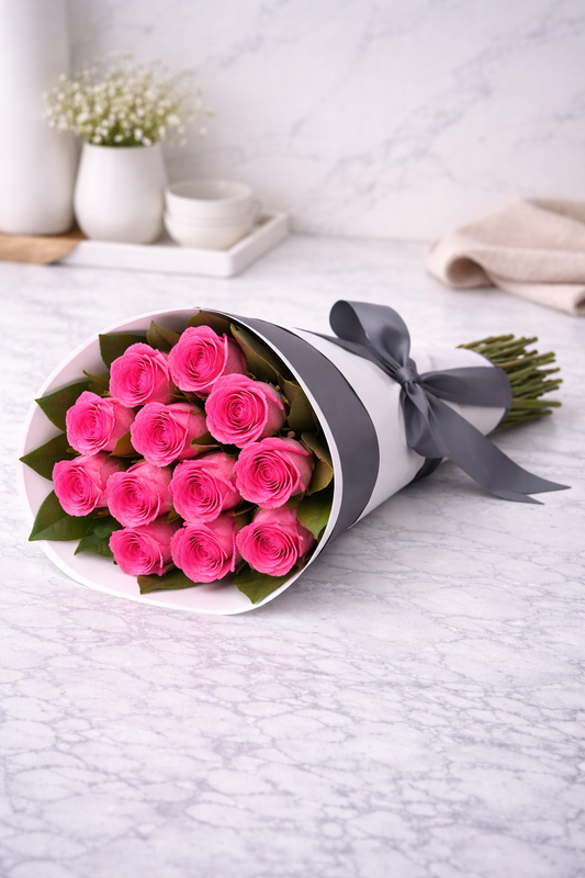 Bouquet of pink roses wrapped in white paper with a gray ribbon on a light surface.